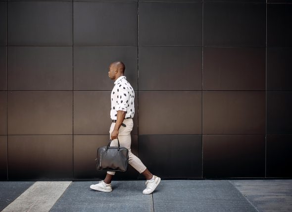 Young handsome businessman walking against black wall in a city