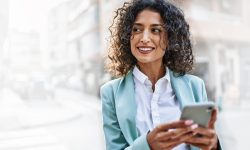 Young hispanic business woman wearing professional look smiling confident at the city using smartphone