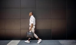 Young handsome businessman walking against black wall in a city